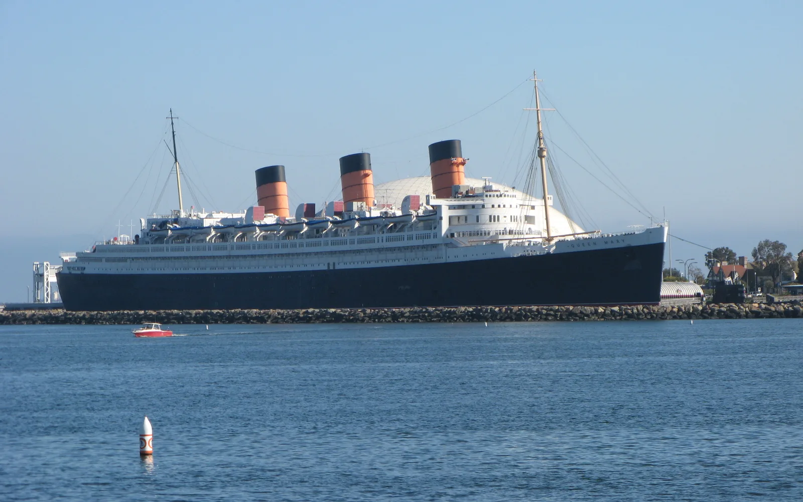 The RMS Queen Mary ocean liner permanently docked at Long Beach, with the ship's white hull and distinctive funnels visible against the waterfront.